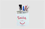 Close-up of adhesive notepaper with smiley face stuck on pen holder over white background