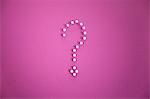 Close-up of push pins forming question mark over pink background