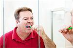Man in his forties brushes his teeth looking in the bathroom mirror.