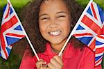 Portrait of a beautiful young smiling happy mixed race interracial girl holding waving British Union Jack Flags, shot outside in summer sunshine