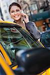 A happy young woman talking on her mobile cell phone by a yellow taxi cab. Shot on location in New York City