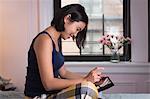 Young woman sitting on bed, using digital tablet