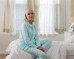 Portrait of sad senior woman sitting on bed wearing pyjamas