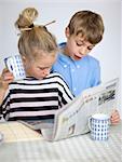 Portrait de garçon et fille lisant journal à table
