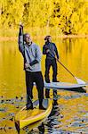 Two people smiling on paddle boards in autumn trees