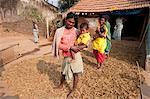 Young father of Desia Kondh tribe holding his son outside his house, standing on crop of drying millet, Bissam Cuttack, Orissa, India, Asia