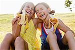 Laughing girls eating bananas outdoors