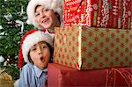 Boys peeking around stack of Christmas presents