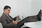Businessman reading newspaper in office with feet up on desk