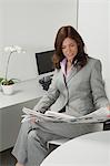 Mature businesswoman reading newspaper in office