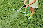 Girl watering lawn with garden hose, cropped