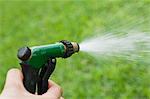 Person using spray nozzle on garden hose to water lawn, cropped