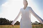 Mid-adult woman standing in field with eyes closed and arms outstretched