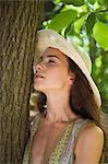 Jeune femme avec un chapeau de soleil appuyé contre le tronc d'arbre, portrait