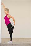 Mature woman stretching against wall, side view