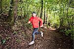 Male trail runner running in the forest on a trail. Red shirt and black pants. Summer season. Slight blur in runner to show motion. Horizontal composition.