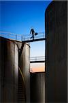 Businessman Crossing Catwalk Between Storage Tanks