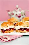 Scones with strawberry jam and cream with a pot of tea in the background