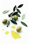A olive sprig with olives next to a pool of olive oil