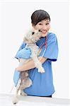 Portrait of Asian female veterinarian cuddling dog over gray background