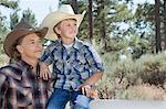 Mature father and son wearing cowboy hats looking away in park