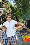 Portrait of a little boy with father barbecuing vegetable on barbecue grill in lawn