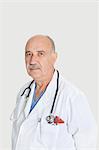 Portrait of serious senior medical practitioner over gray background