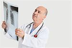 Senior male doctor examining medical radiograph over gray background