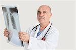 Portrait of senior doctor holding medical radiograph over gray background