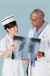 Two medical professionals holding x-ray report while looking at each other over light blue background