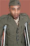 Portrait of African American military officer with crutches, studio shot on brown background