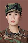 Portrait of young, female soldier in camouflage clothing. Studio shot on brown background