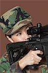 Young female US Marine Corps soldier aiming M4 assault rifle over brown background