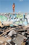 Young woman in bikini standing on graffiti wall with garbage in foreground