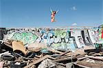 Young woman in bikini jumping over graffiti wall with garbage in foreground