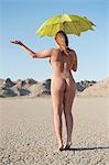 Back view of a naked woman holding umbrella with hand held out on barren landscape