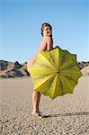 Portrait of a happy naked woman with yellow umbrella on barren landscape