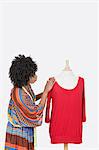 African American female fashion designer looking at red tunic over gray background