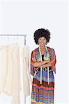 Portrait of an African American female designer with sewing patterns on clothes rack over gray background