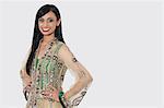 Portrait of an Indian woman in elegant designer wear standing with hands on hips over gray background