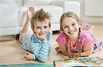 Portrait of happy siblings with story books lying on floor in living room