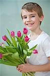 Portrait of happy young boy holding bunch of pink tulips against gray background