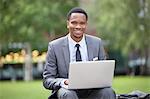 Portrait of a happy African American businessman using laptop in park