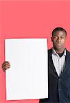 Portrait of a young man holding blank cardboard over pink background