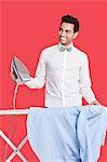 Happy man in formals ironing shirt over red background