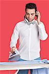 Man ironing cloth while listening music over red background