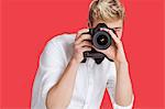 Young man taking picture with digital camera over red background