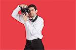 Mixed race man taking picture with digital camera over red background