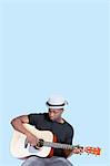 Young African American man playing guitar over light blue background