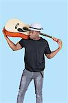 Young African American man carrying guitar over light blue background